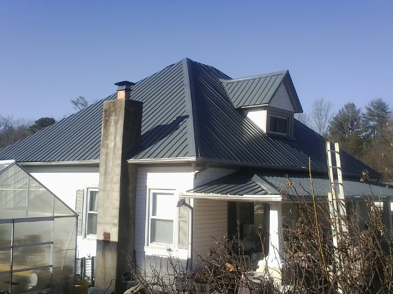 Dark blue standing seam metal roof on a white farmhouse with dormer — Slate & Tile Roof Repair by Roofing Brothers in Letha