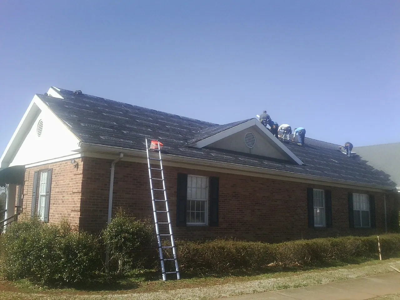 Crew tearing shingles off a brick ranch roof with a ladder set — Metal Roof Repair work by our crew in Letha