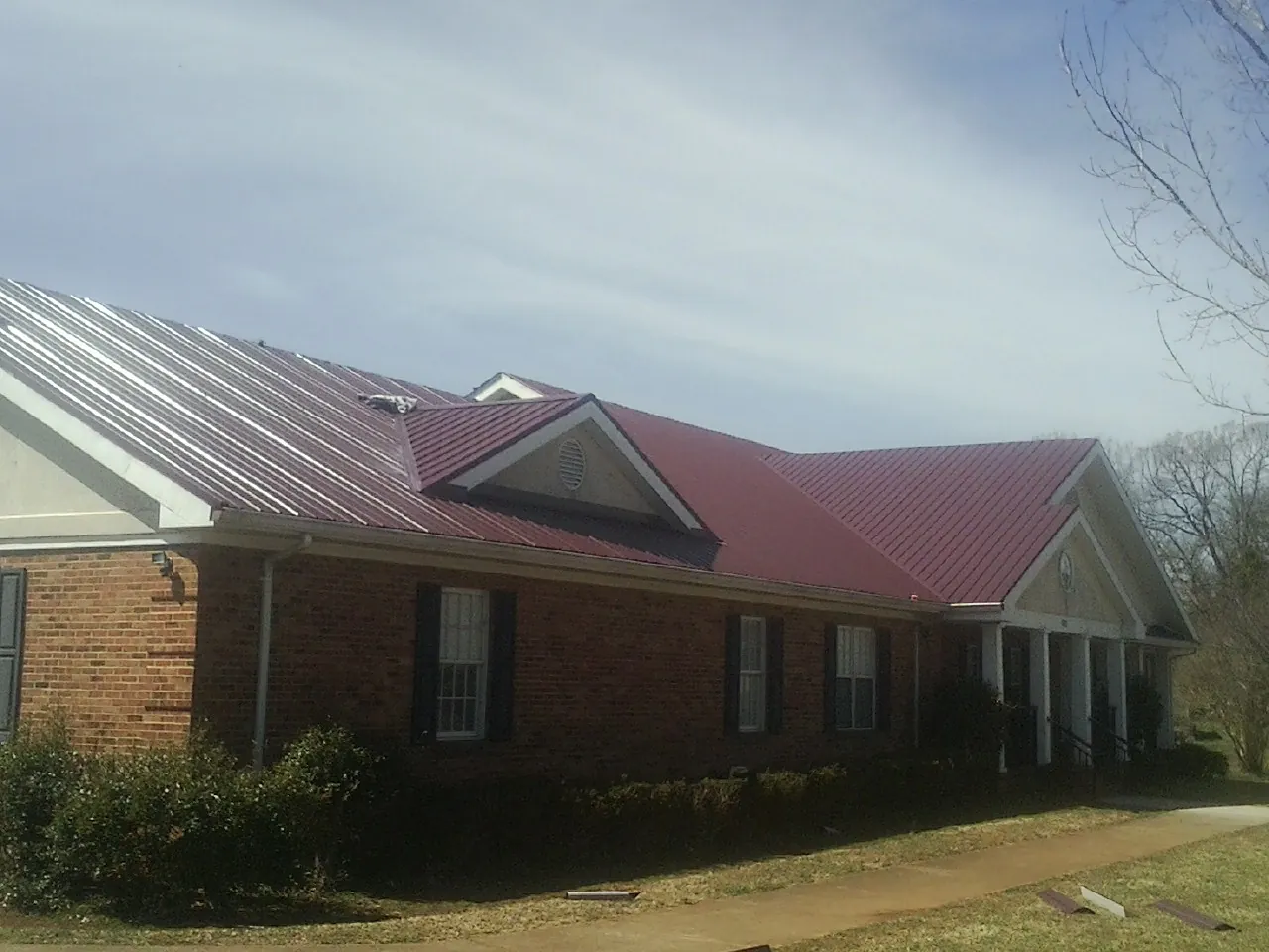 Red metal roof with gabled entries on a long brick building, from a Hail Damage Roof Repair job in Letha