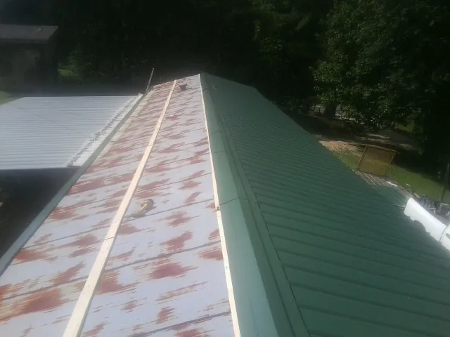 Old rusted panels beside newly installed green metal roofing — Wind Damage Roof Repair by Roofing Brothers in Letha