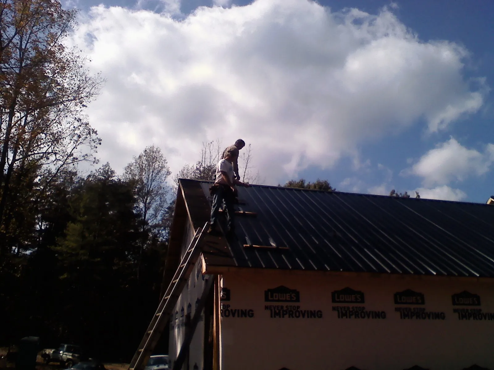 Roofer fastening dark metal panels high against a cloudy sky, from a Roof Inspection job in Letha