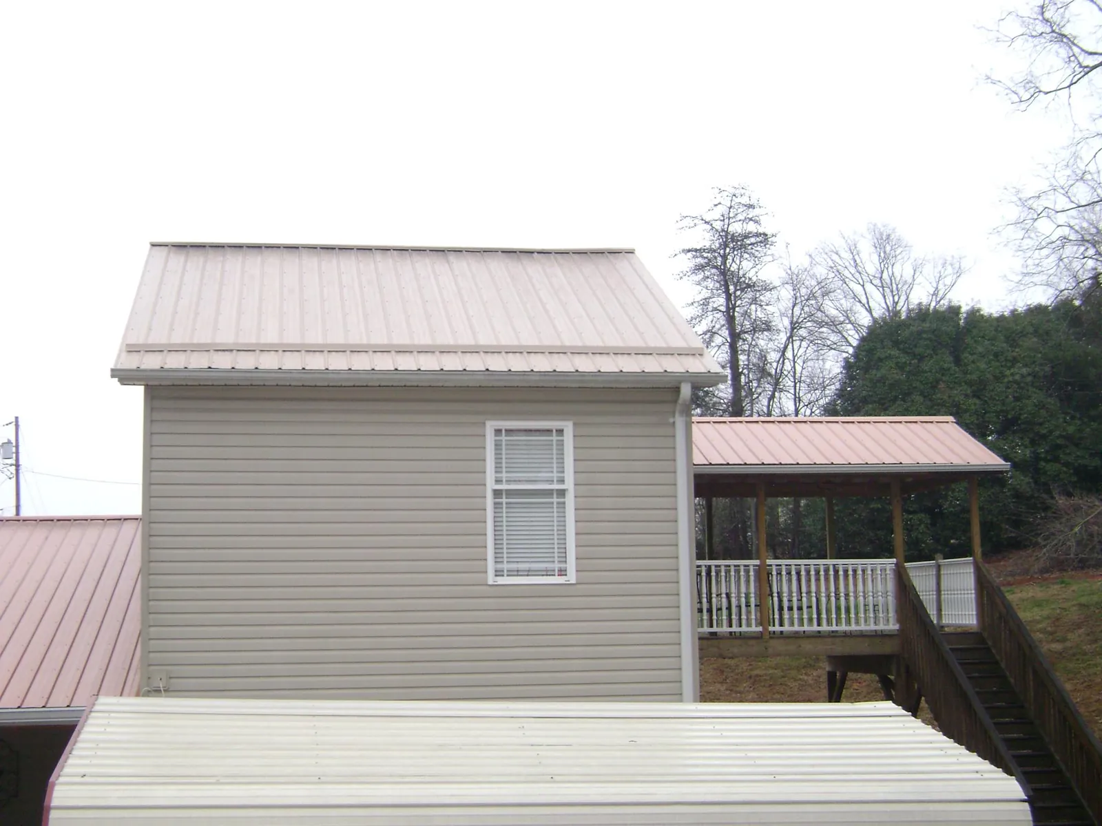 Tan metal roofs on a two story addition and attached porch, from a Roof Replacement job in Letha